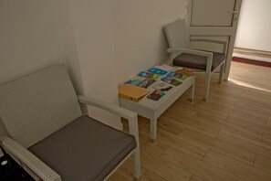 Une pièce comprenant deux fauteuils en osier, dont l’un est doté d’un coussin, ainsi qu’une petite table sur laquelle se trouvent des livres et un classeur.