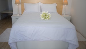A neatly made bed with white linens and a floral centerpiece, flanked by two bedside lamps on white nightstands. - Azores Horta Apartments (Horta)