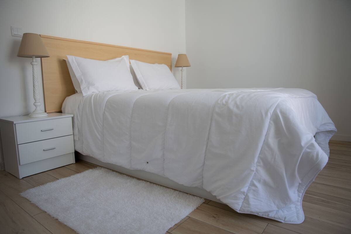 A neatly made bed with white bedding, a white nightstand with drawers, and two bedside lamps.
