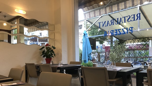 Ein Restaurant mit Außenbereich, Tischen, Stühlen und einem Blumentopf.