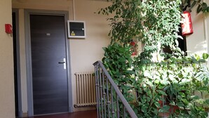 Eine Treppe mit Metallgeländer, eine Tür mit Nummernschild, ein Brandmelder und ein Heizkörper.