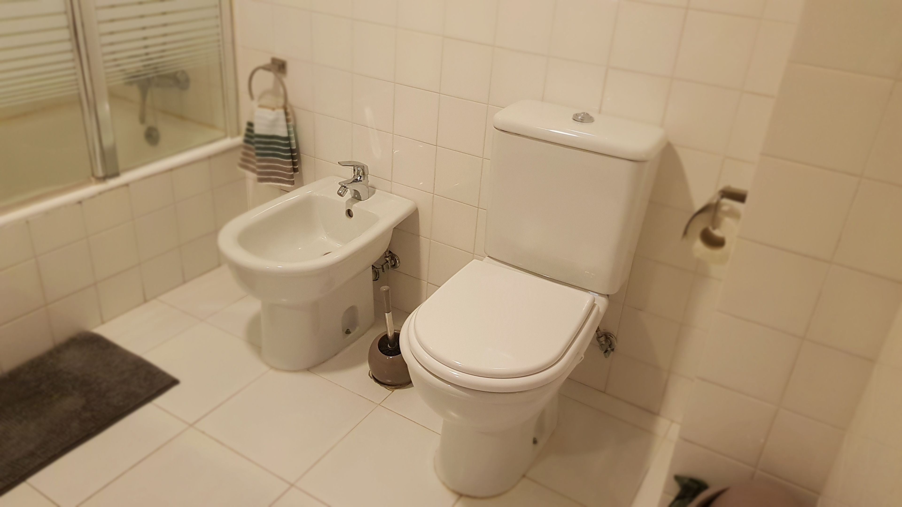 A bathroom with a bidet, toilet, and a window with blinds.