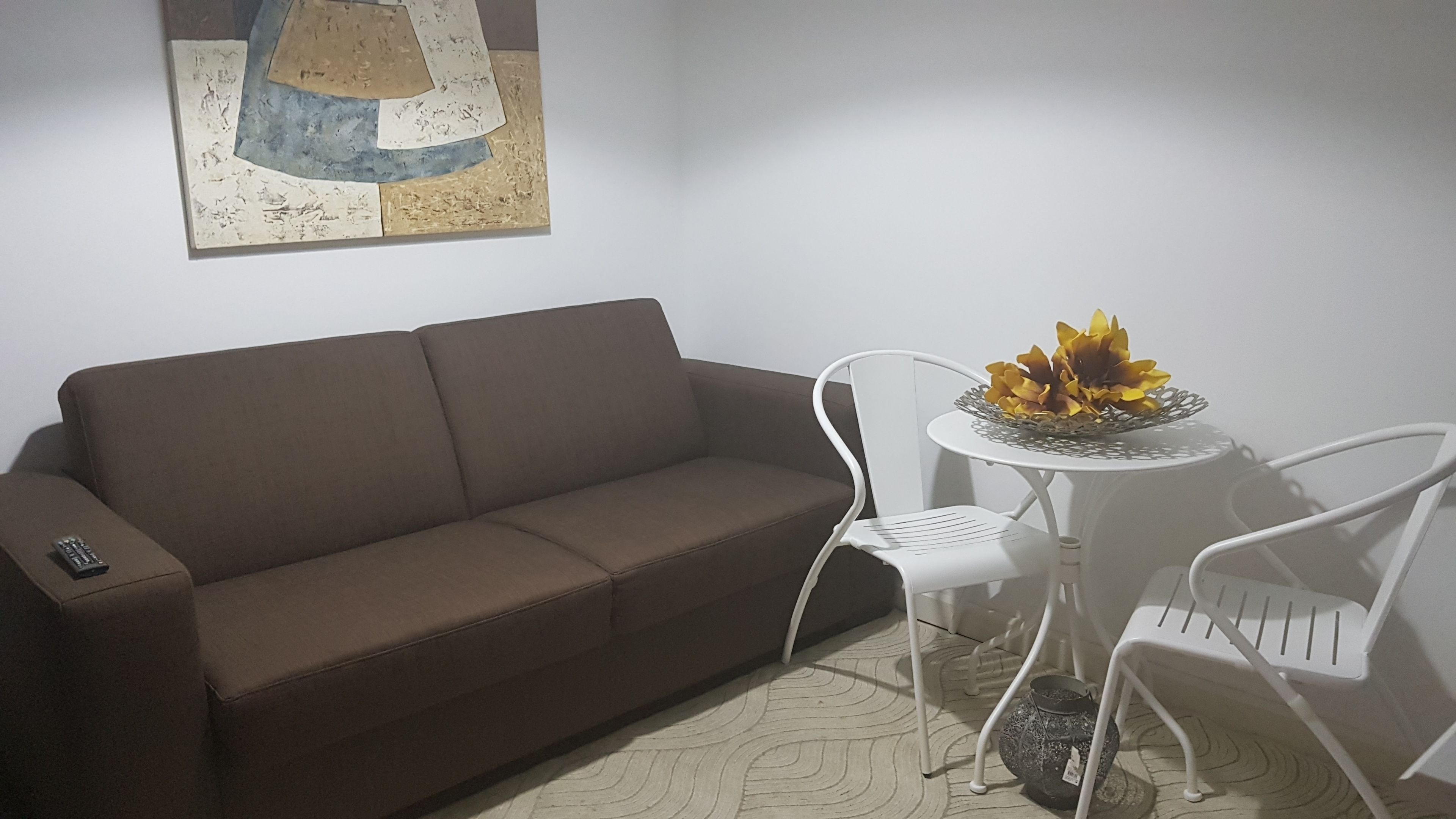 Un divano marrone, una sedia bianca, un tavolino rotondo con una ciotola decorativa e un quadro astratto appeso al muro.