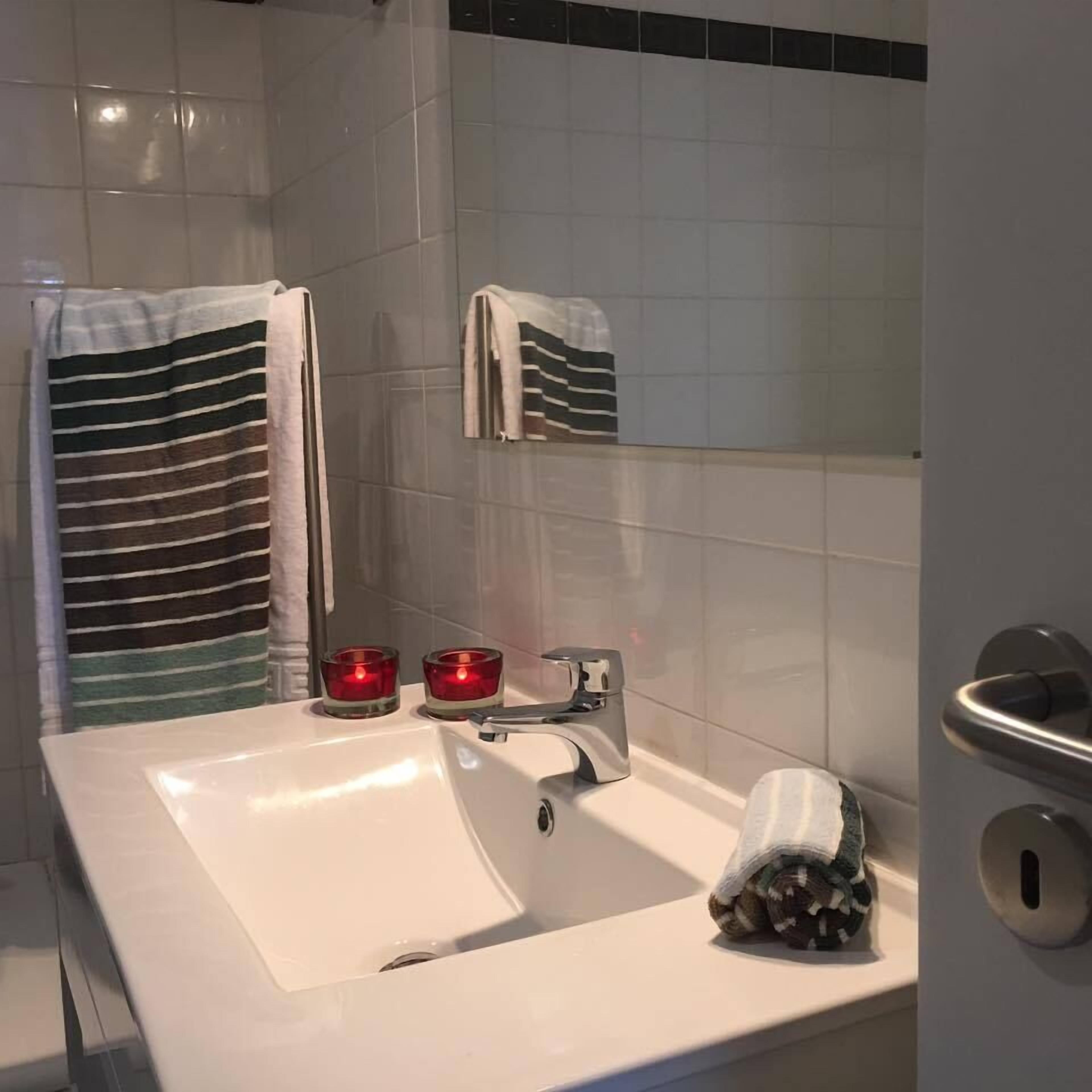 A bathroom with a white sink, two red candles, and towels hanging on the wall.