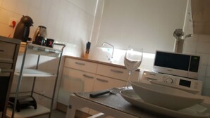 Uma cozinha moderna com armários brancos, micro-ondas, chaleira e uma taça de vinho no balcão.