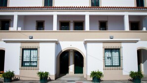 Um edifício de dois andares com telhado plano, paredes brancas e uma entrada central com arco.