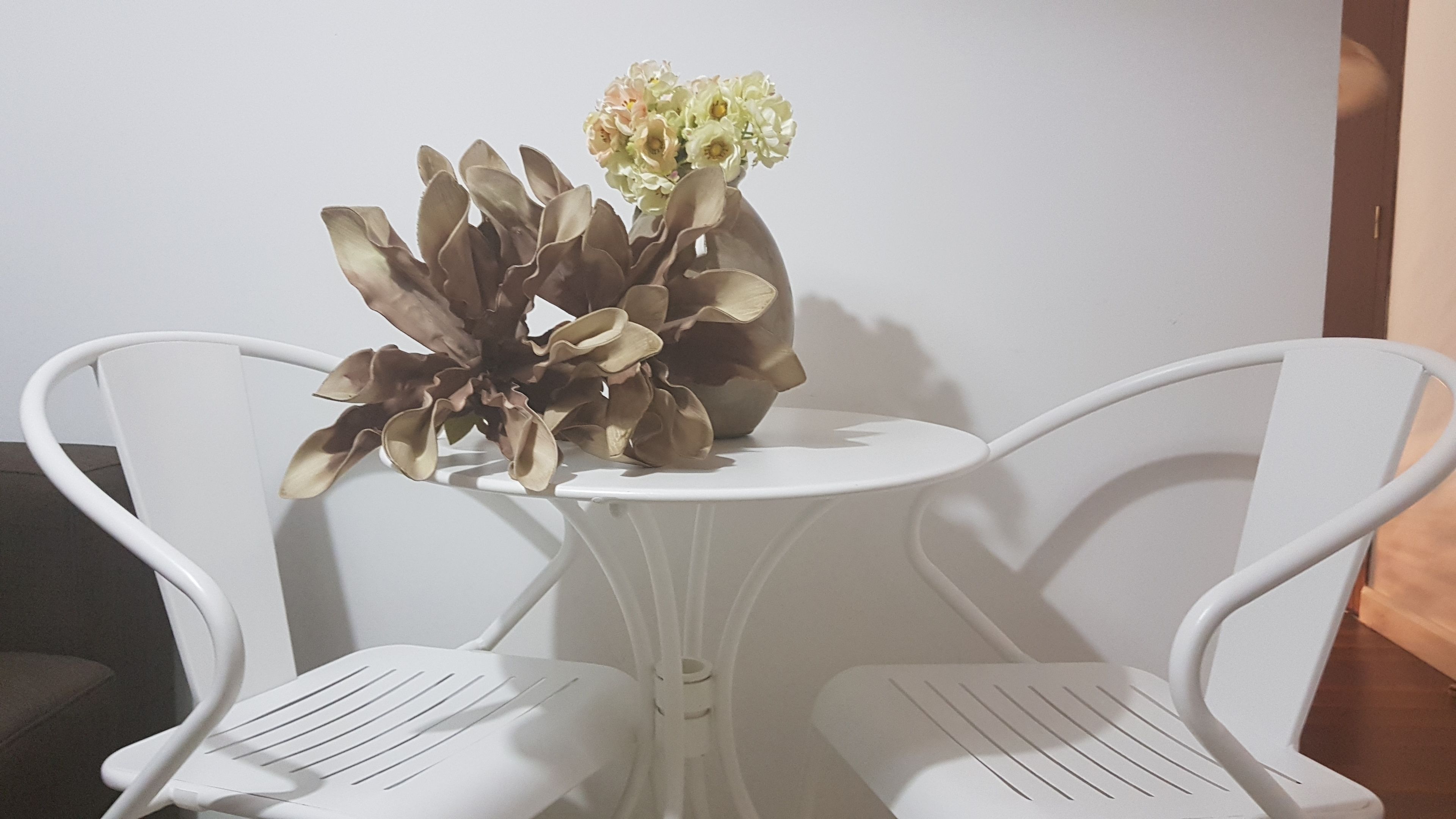 Une petite table blanche avec un vase de fleurs et deux chaises blanches.