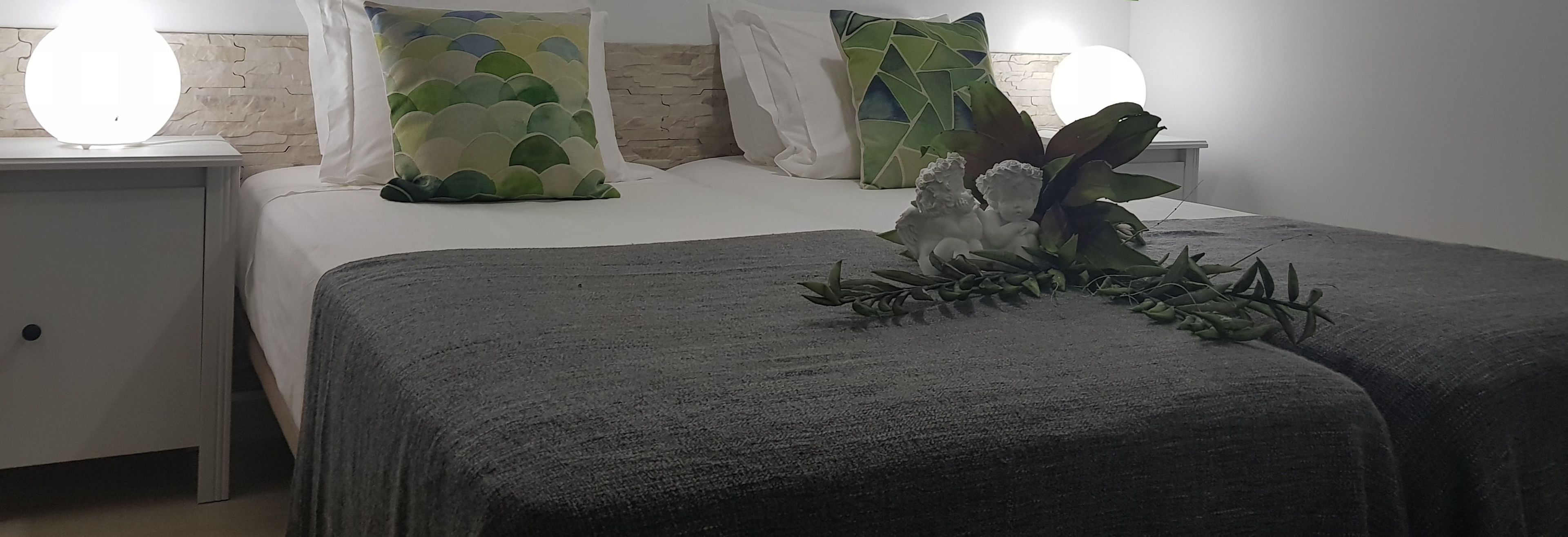 A neatly made bed with a decorative centerpiece, a bedside table with a lamp, and a wall with a textured pattern.
