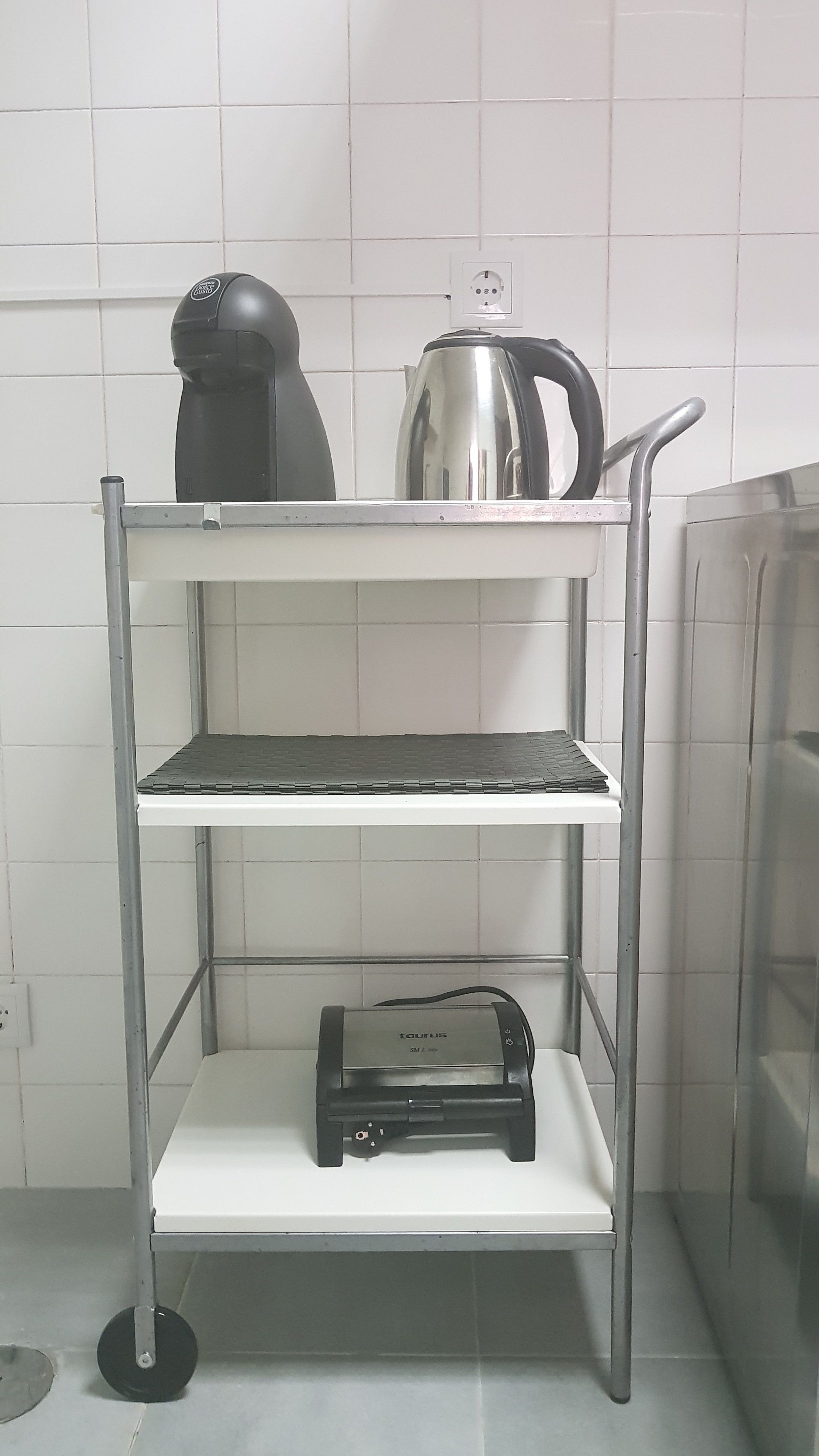 Een metalen schap met een waterkoker, koffiezetapparaat en broodrooster.