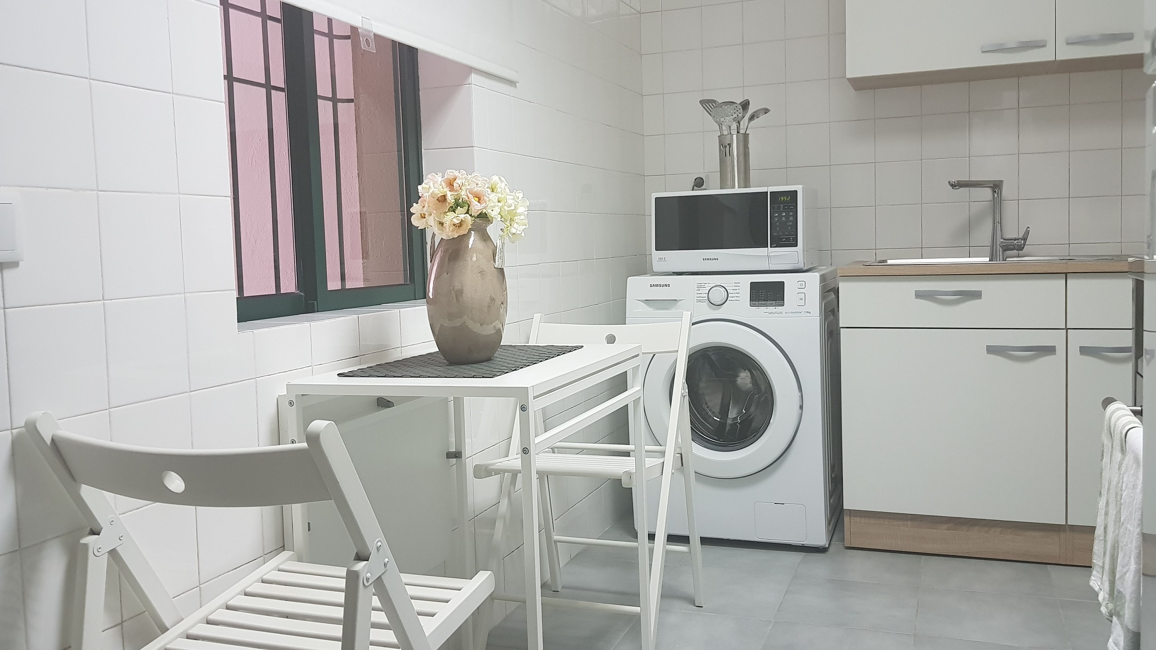 Una cocina pequeña y moderna con electrodomésticos blancos, lavadora, microondas y fregadero.
