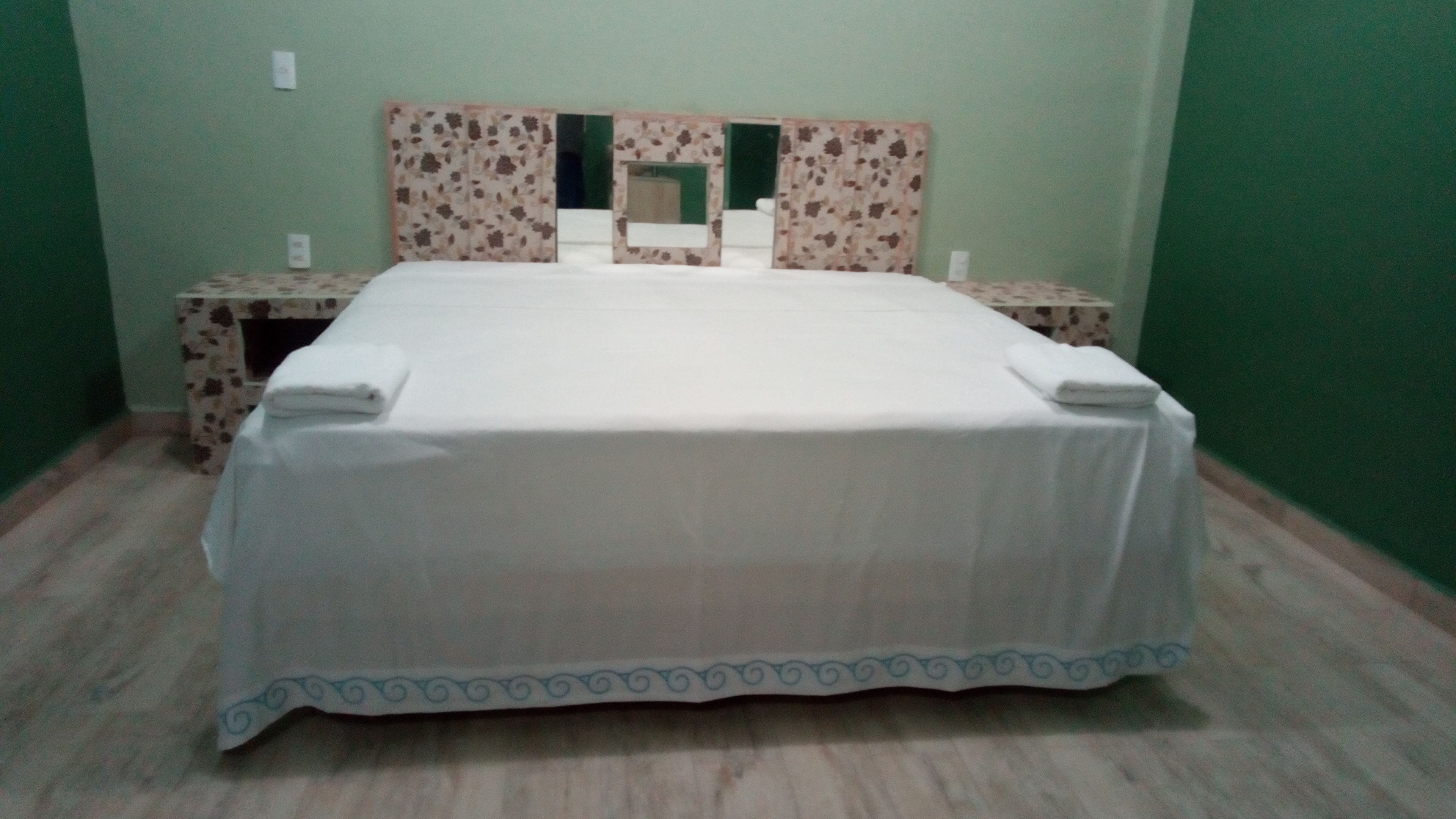 A neatly made bed with a white bedspread and blue trim, flanked by two nightstands with floral-patterned side tables.