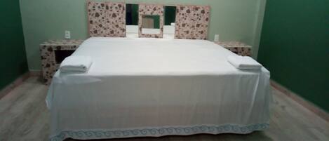 A neatly made bed with a white bedspread and blue trim, flanked by two nightstands with floral-patterned side tables.