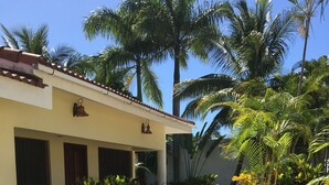 Un bâtiment doté d’un balcon, entouré de plantes tropicales et d’un jardin agrémenté de fleurs rouges.