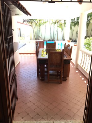 A patio with a tiled floor, a wooden table with chairs, and a view of palm trees and a building in the background.