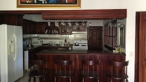 Une cuisine dotée d’un îlot central, de tabourets de bar en bois, d’un réfrigérateur et d’un tableau accroché au-dessus de l’îlot.