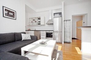 A modern apartment with a grey sofa, white coffee table, and a kitchenette with a microwave and oven.