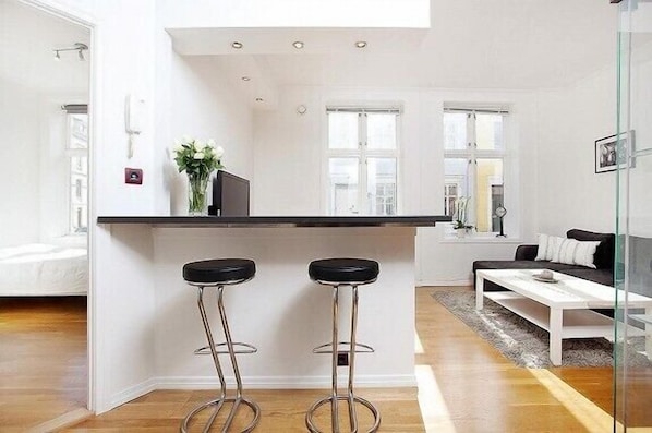A modern kitchen with a central island, two bar stools, and a dining area with a white table and sofa.