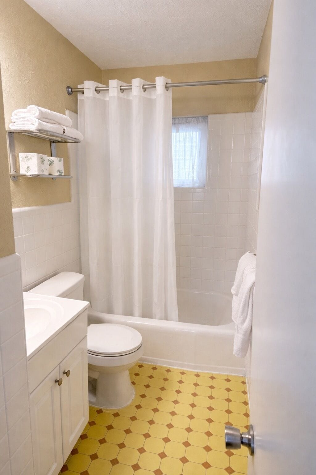 A bathroom with a toilet, sink, shower, and a window.