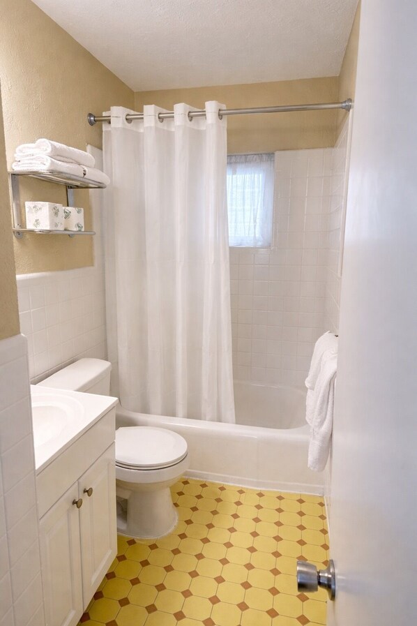 A bathroom with a toilet, sink, shower, and a window. - Beach Colony Motel (Wildwood Crest)