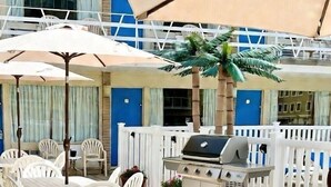 An outdoor patio with white plastic chairs and tables, a grill, and a palm tree.