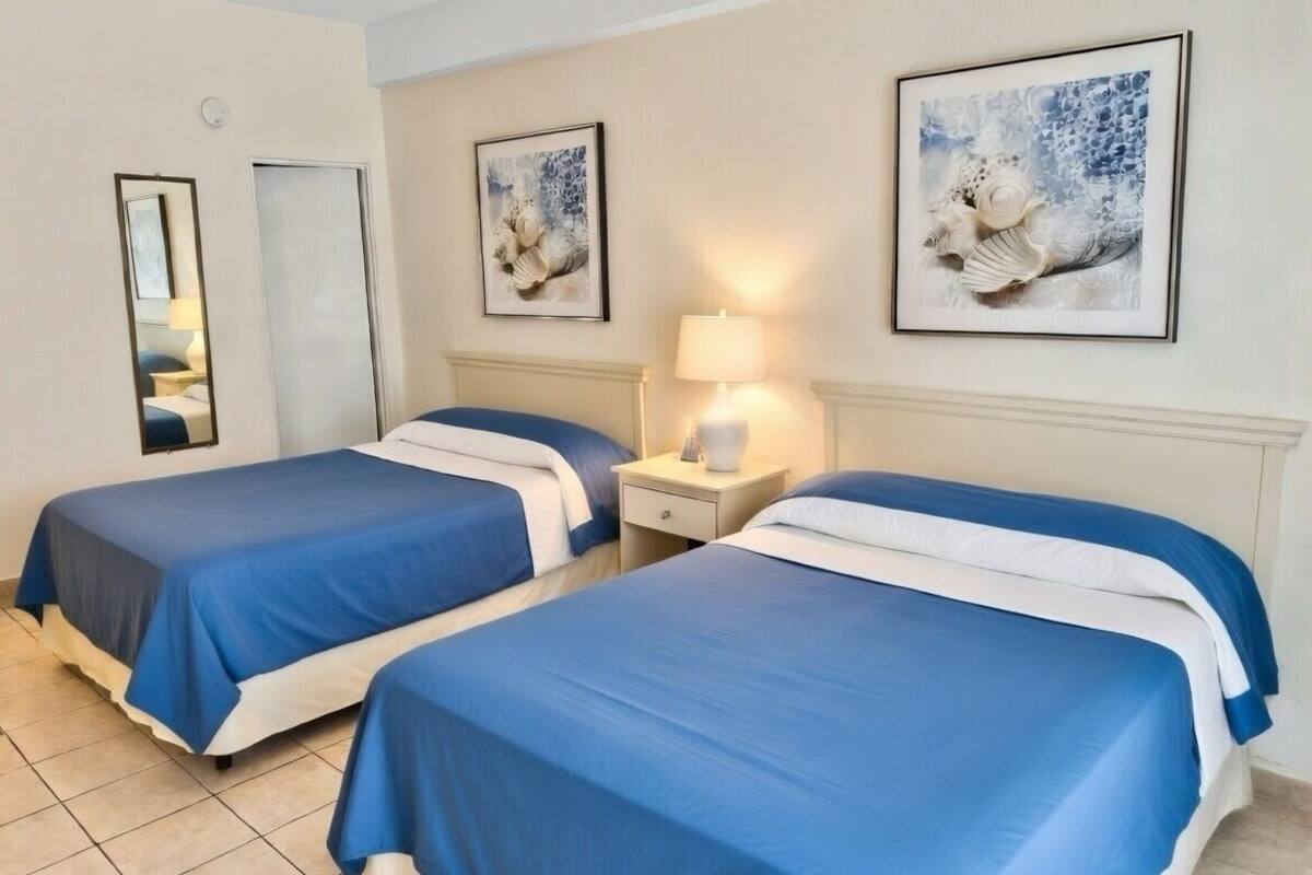 A hotel room with two beds, a nightstand with a lamp, and artwork on the walls.