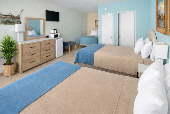 A hotel room with two beds, a desk, a chair, a TV, a dresser, and a plant. - Beach Colony Motel (Wildwood Crest)