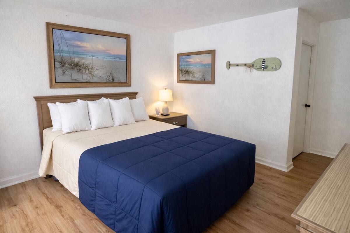 A bedroom with a bed, a nightstand, a lamp, and two framed pictures on the wall.