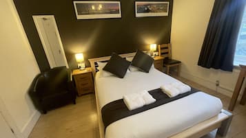 Habitación de hotel impecable con una cama grande, dos mesitas de noche con lámparas, una silla y un escritorio.