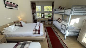 Une chambre d’hôtel avec un grand lit, un lit plus petit, un bureau avec une chaise, un lit superposé et une fenêtre avec des rideaux.