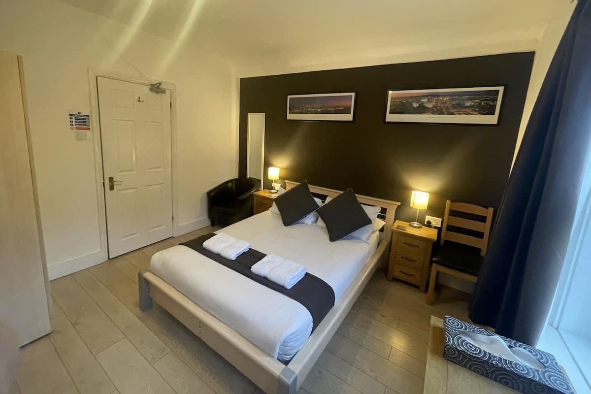 Quarto de hotel com cama, mesas de cabeceira, uma cadeira, escrivaninha, espelho e porta.