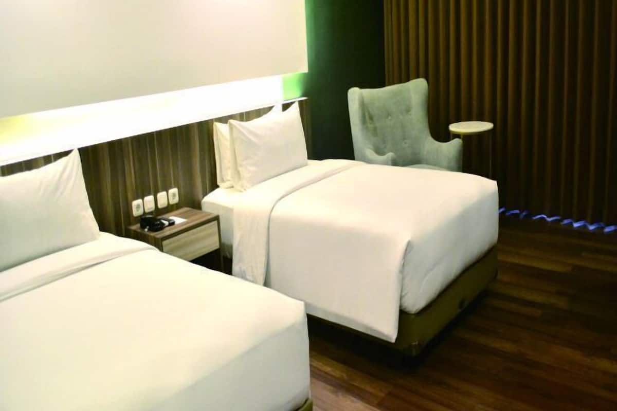 A hotel room with two beds, a nightstand, a lamp, and a chair.