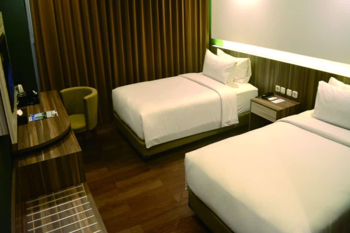 A hotel room with two beds, a desk, a chair, and a nightstand with a phone and a lamp.