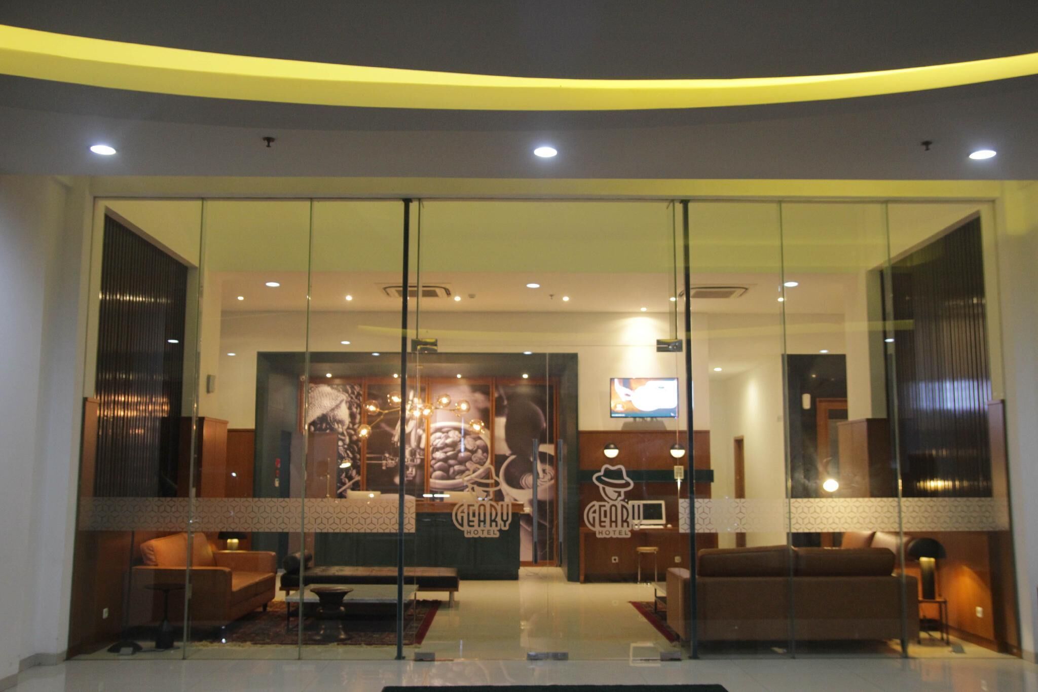 A hotel lobby with a reception desk, seating area, and a large coffee-themed mural.