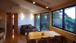 Een modern interieur met een houten eettafel, stoelen, een bank en een groot raam met uitzicht op bomen.