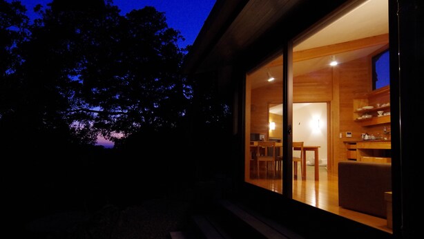 Een modern huis met een groot raam dat een eethoek met houten meubels onthult.