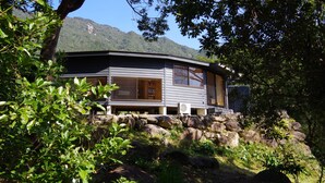 Een modern huis met een groot raam en een deur, omringd door groen en rotsen.