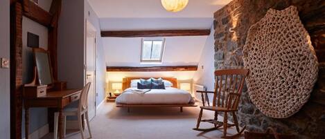 A cozy bedroom with a bed, wooden rocking chair, and a stone wall.