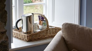 Una habitación con ventana, una bandeja de mimbre con hervidor y bolsitas de té, y una silla.