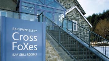 Un bâtiment en pierre doté d’une entrée en verre et d’une enseigne indiquant « Cross Foxes Bar Grill Rooms », accueillant les visiteurs.
