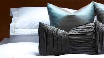 A neatly made bed with a white comforter, a gray blanket, and a beige throw.