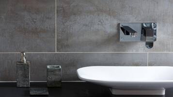 Een moderne badkamer met een witte wastafel, een handdouche en een wandmengkraan.