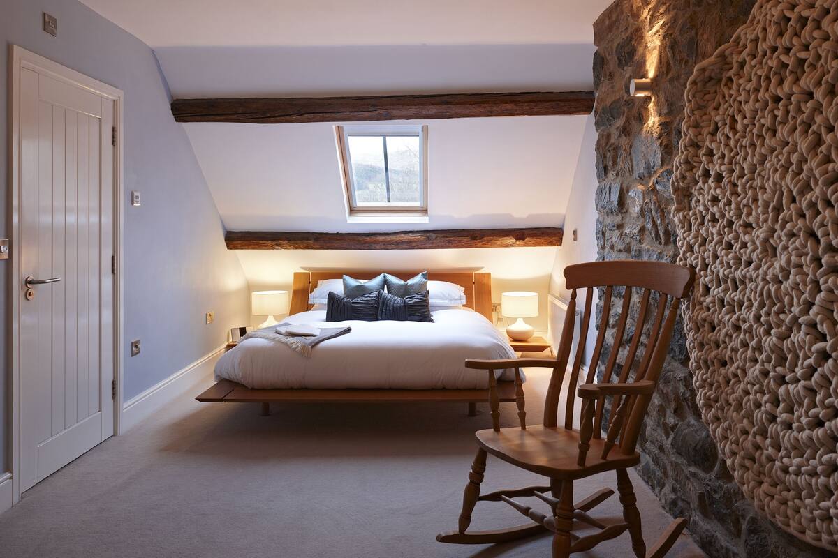 Een slaapkamer met een bed, een schommelstoel, een stenen muur en een raam.