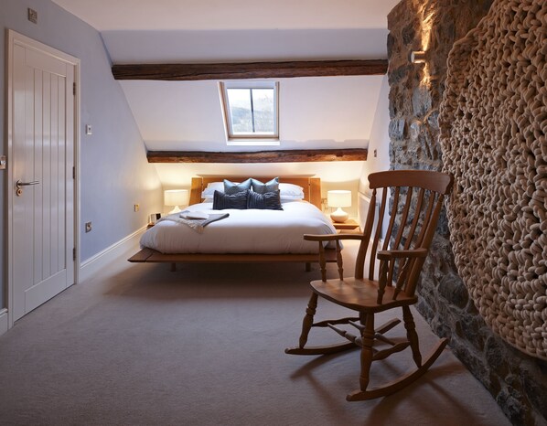 Een slaapkamer met een bed, een schommelstoel, een stenen muur en een raam.
