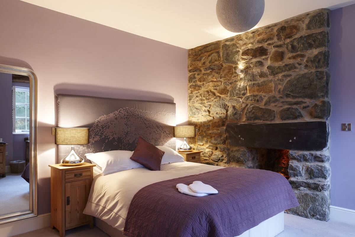 Een slaapkamer met een stenen muur, een bed met een paars deken, twee bedlampen en een hanglamp.