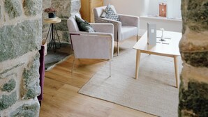 Una sala de estar acogedora con paredes de piedra, techo de madera, un sofá blanco, una mesita y una lámpara.