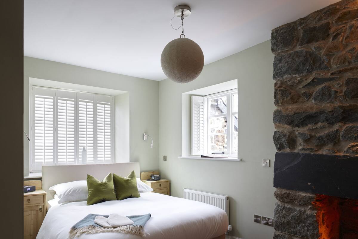 Een slaapkamer met een bed, twee nachtkastjes, een stenen muur en een open haard.