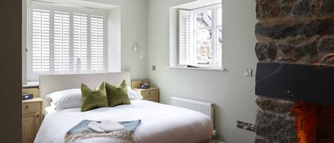 A bedroom with a bed, two nightstands, a stone wall, and a fireplace.