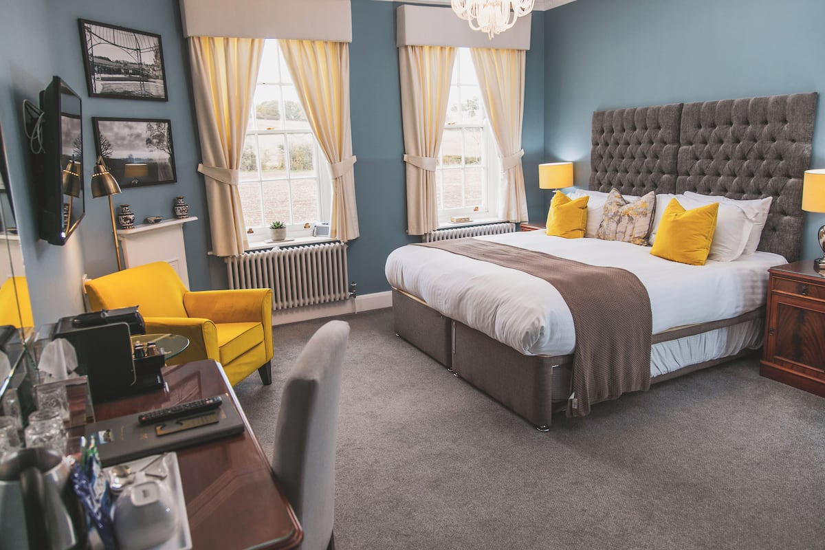 A bedroom with a large bed, a desk with a chair, a yellow armchair, and a radiator.
