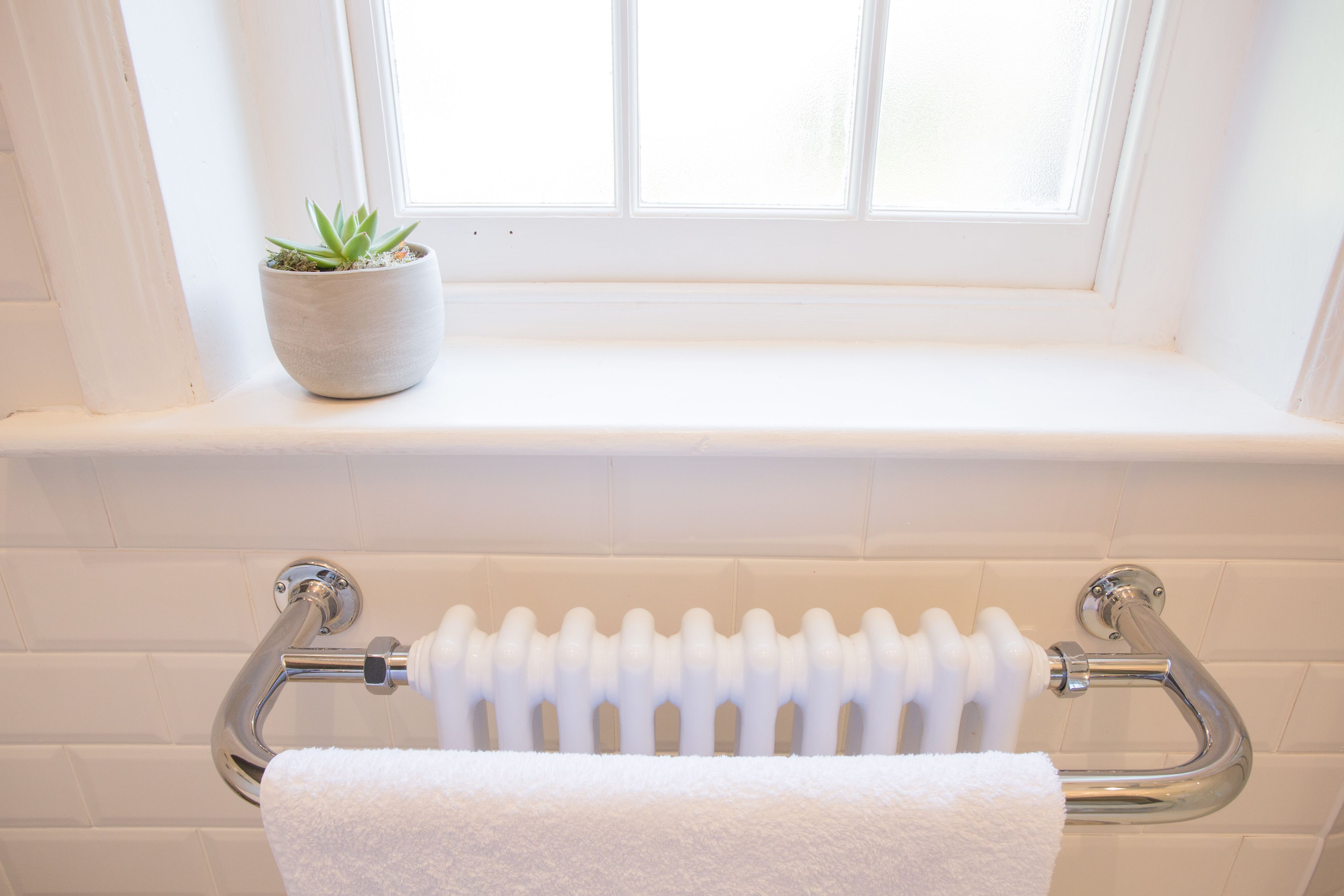 A bathroom with a white radiator, a white towel hanging on a towel rack, and a potted plant on a windowsill.