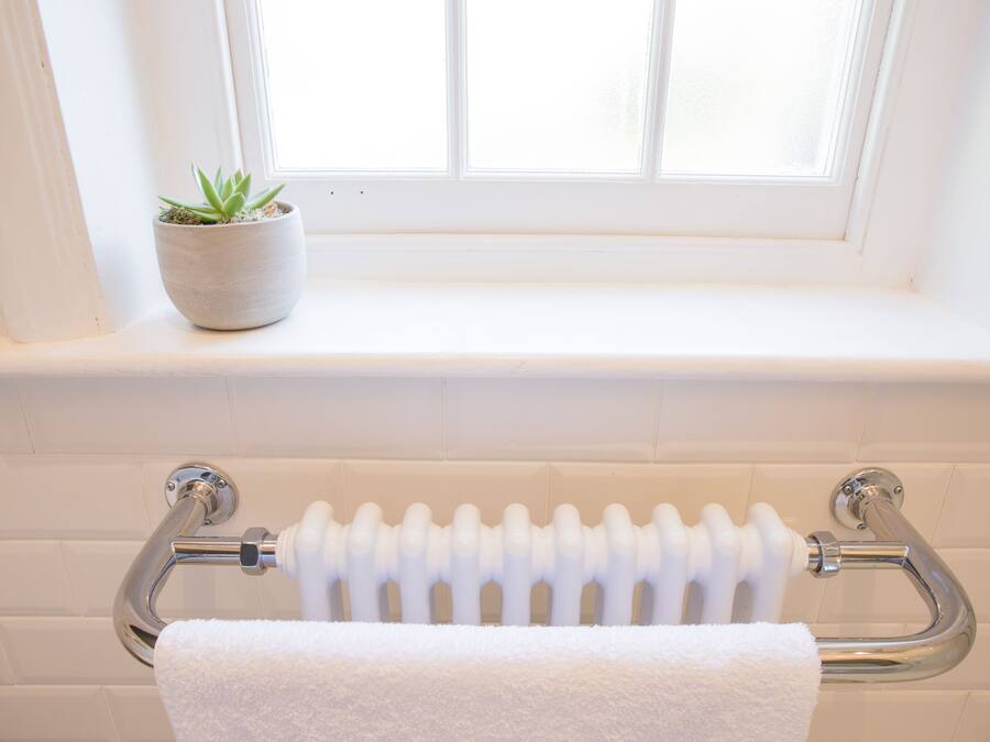 A bathroom with a white radiator, a white towel hanging on a towel rack, and a potted plant on a windowsill.
